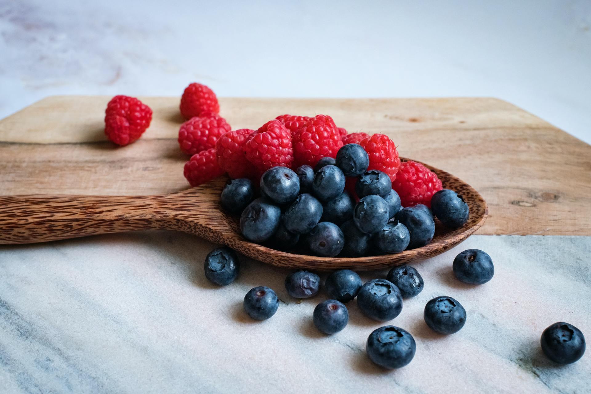 Close-up of fresh raspberries and blueberries on a wooden spoon and cutting board, highlighting fresh, brain-healthy berries.